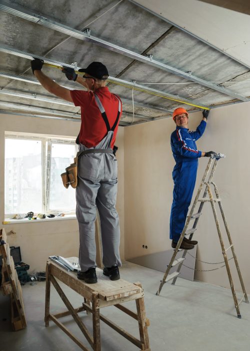 Workers measure metal frame for plasterboard ceilings
